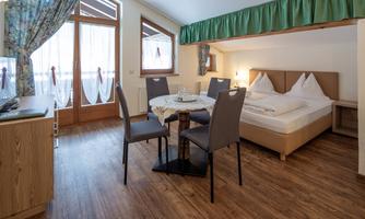 A cozy room with a double bed and a dining table. The room has large windows with beautiful curtains.