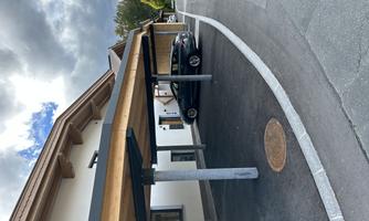 A modern carport in front of a building. In the background, clouds and trees are visible.