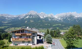 A picturesque landscape with majestic mountains in the background. In the foreground stands a cozy house surrounded by trees and meadows.