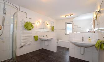 A modern bathroom with two sinks and a walk-in shower. Green towels and accessories add a fresh touch.