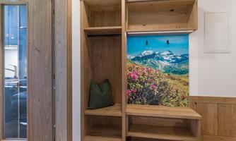 A modern wardrobe area made of wood with a calming landscape wall. The wall features a picturesque mountain landscape with blooming plants.