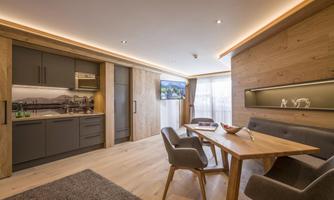 A modern apartment with an open kitchen and a cozy dining area. Bright wooden walls and soft lighting create an inviting atmosphere.