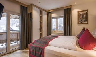 A cozy bedroom with a large bed and red pillows. The room has a bright atmosphere and a balcony overlooking the mountains.