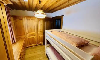 A cozy bedroom with a loft bed and a wooden dresser. The walls are adorned with warm wooden beams and soft lighting.