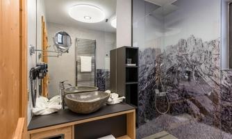 A modern bathroom with a large, stylish washbasin and a glass shower. An impressive mountain motif can be seen on the wall.