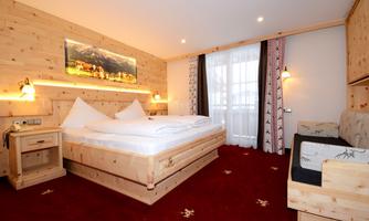 A cozy hotel room with wooden decor and a large double bed. The room has a warm ambiance and a nice view through the window.