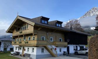 A charming wooden house with two floors and a lovely balcony. In the background, there are mountains and a clear sky.