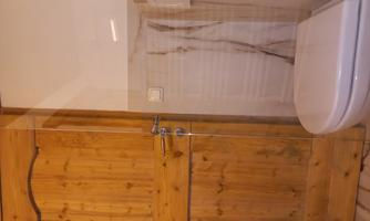 A modern bathroom with a wooden bath door and a white toilet. The walls are elegantly adorned with marbled tiles.