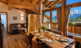 A modern dining room with a large table and colorful chairs. Large windows provide a view of the mountains and let in plenty of daylight.