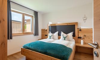 A cozy bedroom with a wooden bed and green bedspread. Large windows provide plenty of daylight and an inviting atmosphere.