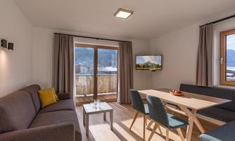 A modern living room with a cozy sofa and a dining area. Large windows offer a view of the surroundings and provide pleasant light.