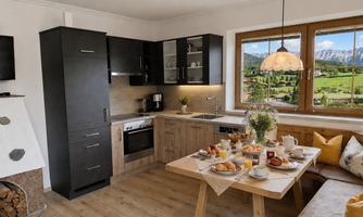 A modern kitchen with an inviting dining area. The table is richly laid out with breakfast specialties and offers a beautiful view of the mountains.