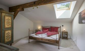 A cozy bedroom with a double bed, red pillows, and a skylight. An antique wardrobe and a bedside table complement the decor.
