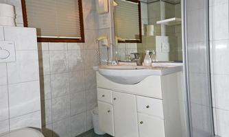 A modern bathroom with white tiles and a sink. There is a shower and a large mirror above the sink.
