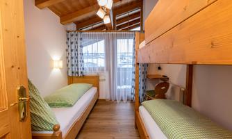 A cozy bedroom with two single beds and a wooden loft bed. Large windows provide plenty of light and a pleasant atmosphere.