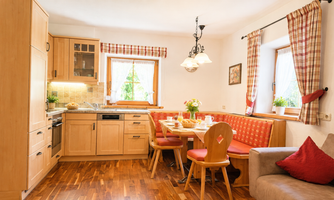 A cozy kitchen with warm wood tones and an inviting dining area. On the table are breakfast dishes and fresh flowers.