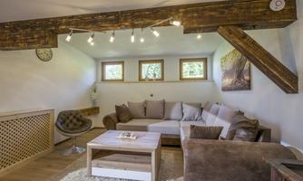 A cozy living room with a light couch and a wooden table. The warm lights and windows create an inviting atmosphere.