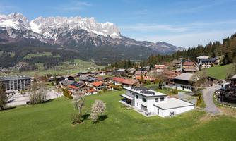 A picturesque landscape with snow-capped mountains and a quiet village. The houses are surrounded by green meadows and trees.