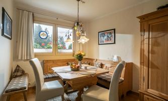 A cozy dining room with a wooden table and white chairs. Large windows let in plenty of light and offer a view of the greenery.
