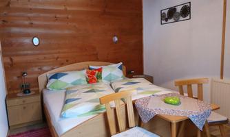 A cozy bedroom with a double bed, colorful pillows, and wood paneling. A small table with two chairs stands next to it, offering an inviting place to relax.