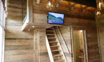 A cozy interior with wooden walls and a staircase. A television displays a landscape while soft lighting creates an inviting atmosphere.