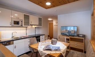 A modern apartment with an open kitchen and dining area. The space is bright and inviting, with a television and comfortable furniture.
