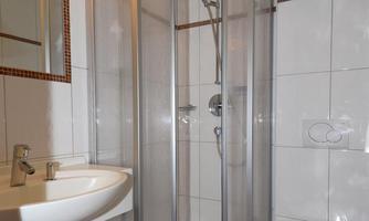 A modern bathroom with a shower cabin and a sink. The walls are tiled and the lighting is pleasant.