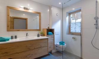 A modern bathroom with a wooden vanity and a large mirror. The shower is open, and there are blue towels on the sink.