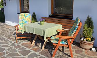 A cozy outdoor area with a table and two chairs. On the table is a plant arrangement, and the surroundings are bright and inviting.