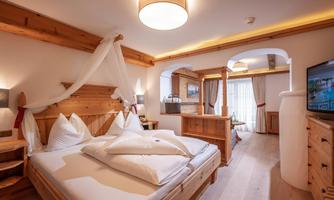 A cozy bedroom with wooden furniture and a large bed. Large windows let in plenty of light.