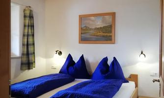 A cozy bedroom with two single beds and blue bedspreads. The walls are bright and the room has wooden details.