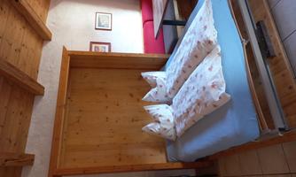 A cozy room with a wooden loft bed and two stacked pillows. The room has a warm atmosphere and features a dining area with a table and chairs.