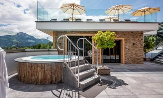 A modern terrace with a whirlpool and sun umbrellas. In the background, mountains and a clear sky are visible.