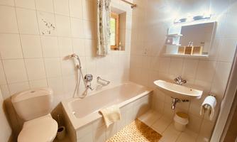 A modern bathroom with a bathtub, a sink, and a toilet. Bright tiles and a window create a friendly atmosphere.