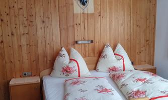 A cozy bedroom with wooden walls. The bed is decorated with beautiful, floral pillows and blankets.