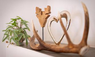 A decorative arrangement with a wooden piece in the shape of antlers, a heart-shaped object, and a green plant branch. The items are on a simple shelf.