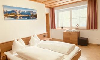 A cozy bedroom with a double bed and a wooden ceiling. A beautiful curtain hangs at the window and a landscape picture adorns the wall.