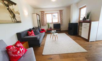 A modern living room with a gray couch and red cushions. A rug and a table complement the cozy atmosphere.