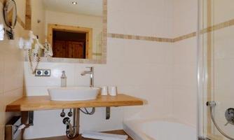 A modern bathroom with a bathtub and a wooden sink. The walls are brightly tiled and there is good lighting.