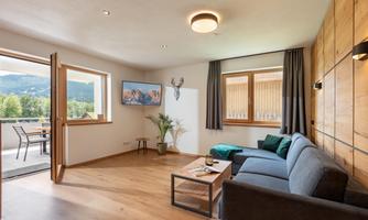 A modern living room with a cozy sofa and a table. Large windows provide a view of nature outside.