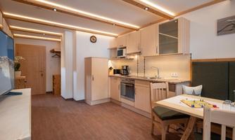 A cozy kitchen with modern furniture and warm lighting. The room includes a dining area and is well-equipped.
