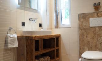 A modern bathroom with a wood drawer for towels and a large mirror. The walls are brightly tiled, and there is a window for natural light.