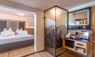A modern hotel room with a large bed and a stylish glass shower. The wooden floor and warm colors create a cozy atmosphere.