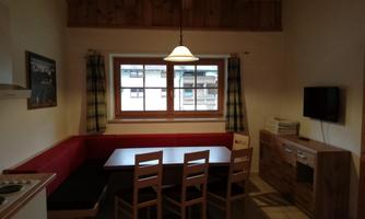 A bright kitchen with a large dining table and chairs. A window lets in a lot of daylight and there are wooden furniture.