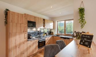 A modern kitchen with wooden furniture and practical appliances. The room is bright and friendly with a view of the garden.