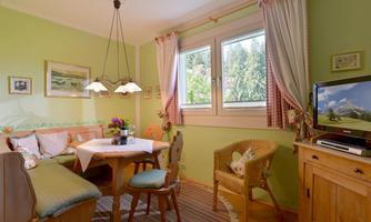 A cozy dining area with a green wall and a table. Large windows let in plenty of light and there is a nice view outside.