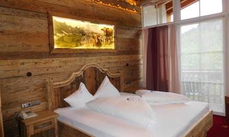 A cozy bedroom in rustic style with wooden paneling. The bed has large, white pillows and the room offers a view of nature through large windows.