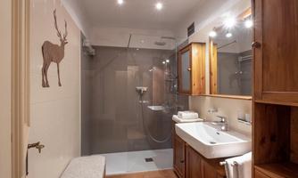 A modern bathroom with a shower and wooden shelves. The decor is bright and inviting, featuring a sink and a seating area.