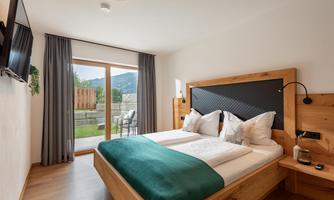 A modern bedroom with a large double bed and wooden furniture. The room has access to a terrace with a view of nature.