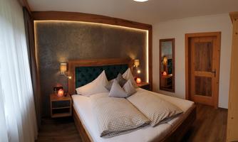 A modern bedroom with a large bed and cozy pillows. The warm wood details and soft lighting create an inviting atmosphere.